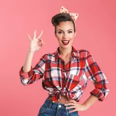 Uśmiechnięta kobieta w stylu pin-up, w kratowanej koszuli i dżinsach, pokazuje znak "OK".