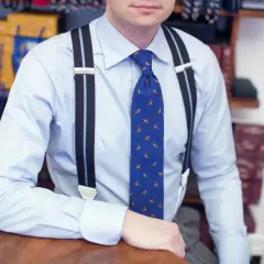 Elegancki mężczyzna w błękitnej koszuli i krawacie z ptakami, pokazuje, jak nosić szelki.