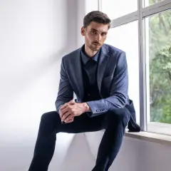 Elegancki mężczyzna w granatowej koszuli i garniturze, zastanawia się, jakie spodnie do niebieskiej koszuli będą najlepsze.