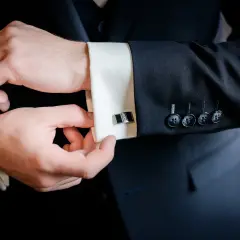 Mężczyzna zapina mankiet koszuli, pokazując, jak założyć spinki do koszuli. Elegancki detal dopełnia stylizację.