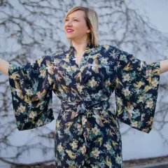 Kobieta w kimonie w styl orientalny, z motywem ptaków i kwiatów, rozkłada ramiona.