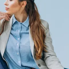 Elegancka kobieta w jasnej marynarce i błękitnej koszuli męskiej, tworząca stylową, biznesową stylizację.