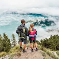 Para w trekkingowych stylizacjach podziwia letni krajobraz górski z jeziorem w chmurach.