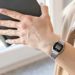 Dłoń kobiety z zegarkiem Casio na nadgarstku, trzymająca ciemną książkę.