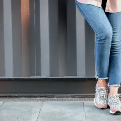 Nogawki jeansów postrzępione na dole, modne sneakersy z błyszczącymi detalami.