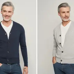 Mężczyzna w granatowym i szarym swetrze rozpinanym na białej koszulce i dżinsach.