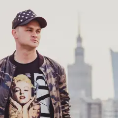 Młody mężczyzna w czapce z daszkiem i bluzie z Marilyn Monroe. Pokazuje, jak nosić czapkę z daszkiem w miejskim stylu.