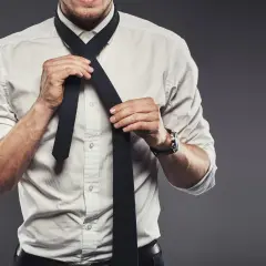 Mężczyzna w białej koszuli wiąże czarny krawat. Prawidłowa długość krawata to klucz do eleganckiego wyglądu.