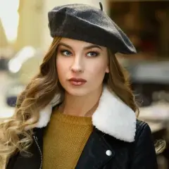 Elegancka kobieta w grafitowym beretu damskim, z burzą blond loków i w skórzanej kurtce. Inspiracja, jak nosić beret damski.