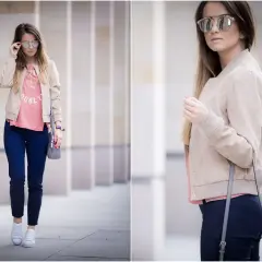 Kobieta w beżowej kurtce bomber, różowym T-shircie i granatowych spodniach, w okularach przeciwsłonecznych.