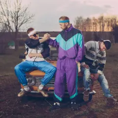 Trzech mężczyzn w dresach i okularach przeciwsłonecznych siedzi na masce starego samochodu. Stylizacja rodem z lat 90. xx wieku.