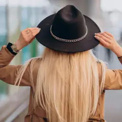 Kobieta w beżowym płaszczu i czarnym kapeluszu z ozdobnym łańcuszkiem. Różne rodzaje kapeluszy damskich mogą podkreślać styl.