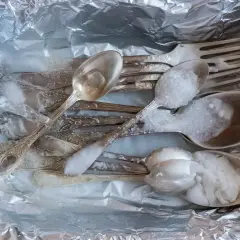 Srebrne sztućce z czarnym nalotem wkładane do folii aluminiowej, zalewane gorącą wodą z solą.