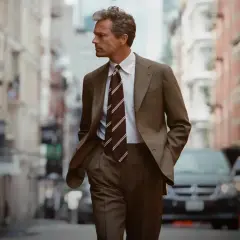 Mężczyzna w eleganckim garniturze, z nonszalancją w rękach w kieszeniach, idzie ulicą. Jego styl to kwintesencja sprezzatury.
