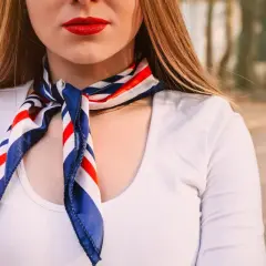 Kobieta w białej koszuli i apaszce w paski. Dowiedz się, jak nosić apaszkę do koszuli, by wyglądać stylowo.