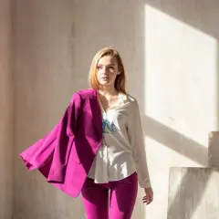Kobieta w stylizacji viva magenta, z marynarką narzuconą na ramię, stoi w świetle słonecznym.