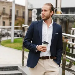 Mężczyzna w stylu smart casual z kawą w ręku, ubrany w granatową marynarkę i jasne spodnie, idzie po schodach.