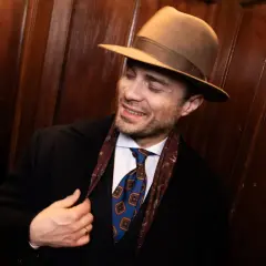 Elegancki mężczyzna w brązowym kapeluszu, czarnym płaszczu i stylowym krawacie. Pokazuje, jak nosić kapelusz męski, dodając klasy każdej stylizacji.