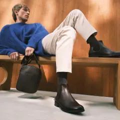 Eleganckie, ciemne botki to idealne buty do chinosów i koszuli. Mężczyzna w niebieskim swetrze prezentuje stylowy zestaw.