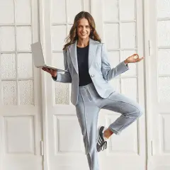 Kobieta w jasnoniebieskim garniturze i sneakersach, trzymająca laptopa, w pozie jogi. Styl casual.