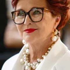 Elegancka kobieta w okularach i bogatej biżuterii z pereł. Pokazuje, jak nosić perły, by wyglądać szykownie.