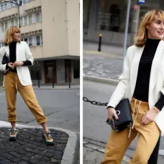 Modna kobieta w stylizacji z czarnym golfem, białej marynarce i musztardowych spodniach dresowych.