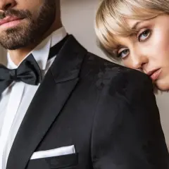 Elegancki mężczyzna w czarnym smokingu z muchą i białą koszulą. Kobieta opiera głowę na jego ramieniu. Idealny przykład, jaka koszula do muchy.