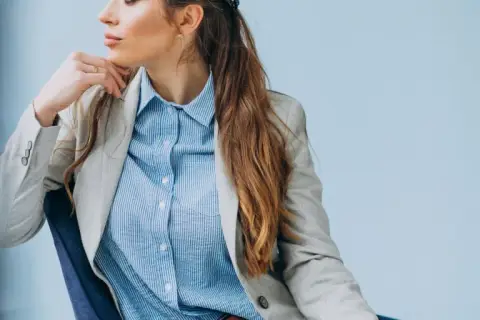 Elegancka kobieta w jasnej marynarce i błękitnej koszuli męskiej, tworząca stylową, biznesową stylizację.