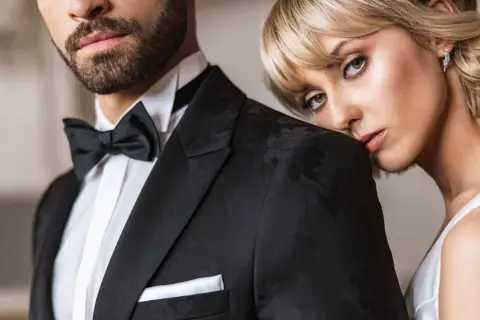 Elegancki mężczyzna w czarnym smokingu z muchą i białą koszulą. Kobieta opiera głowę na jego ramieniu. Idealny przykład, jaka koszula do muchy.
