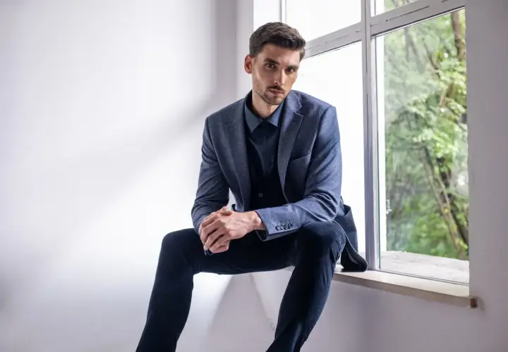 Elegancki mężczyzna w granatowej koszuli i garniturze, zastanawia się, jakie spodnie do niebieskiej koszuli będą najlepsze.