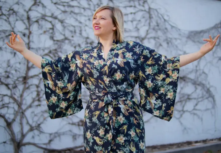 Kobieta w kimonie w styl orientalny, z motywem ptaków i kwiatów, rozkłada ramiona.