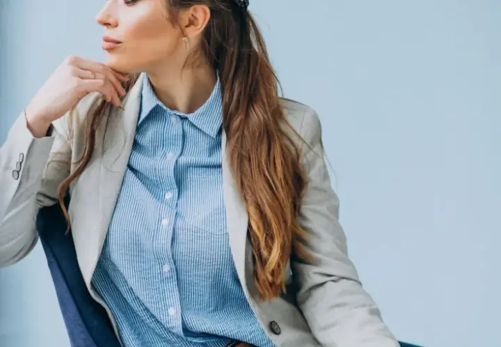 Elegancka kobieta w jasnej marynarce i błękitnej koszuli męskiej, tworząca stylową, biznesową stylizację.