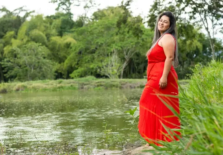 Kobieta w czerwonej sukience, która świetnie sprawdzi się jako jaka sukienka dla niskiej osoby z brzuszkiem. Stoi nad jeziorem, otoczona zielenią.