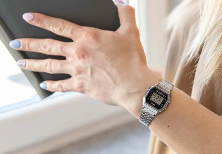 Dłoń kobiety z zegarkiem Casio na nadgarstku, trzymająca ciemną książkę.