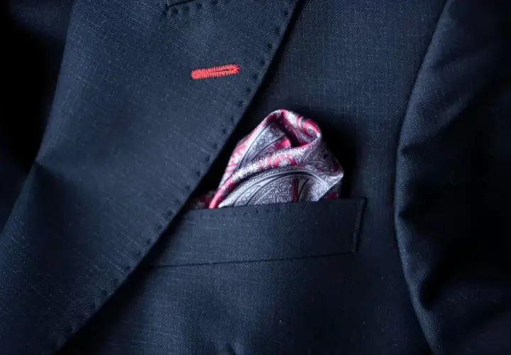 Elegancka poszetka w paisley do granatowego garnituru, z subtelnym czerwonym przeszyciem na klapie.