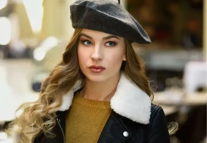 Elegancka kobieta w grafitowym beretu damskim, z burzą blond loków i w skórzanej kurtce. Inspiracja, jak nosić beret damski.