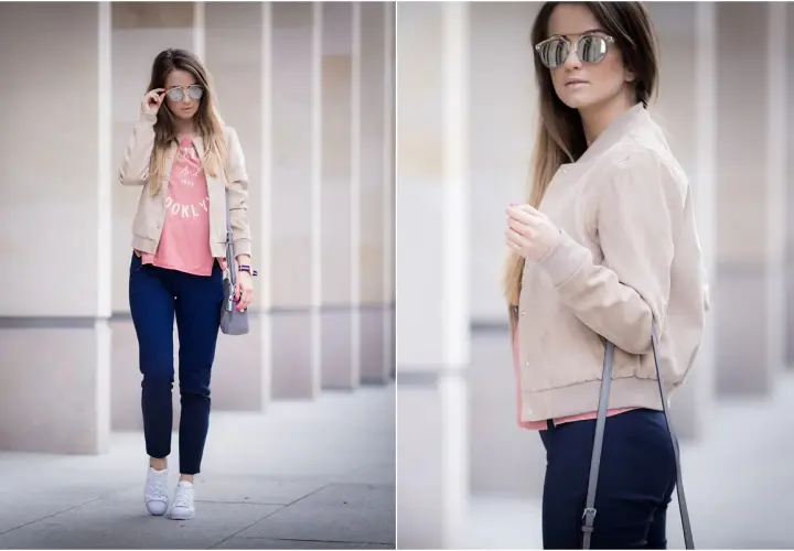 Kobieta w beżowej kurtce bomber, różowym T-shircie i granatowych spodniach, w okularach przeciwsłonecznych.