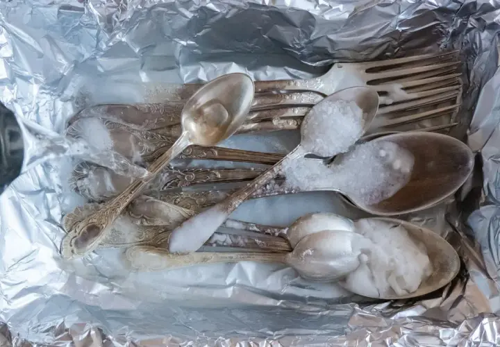 Srebrne sztućce z czarnym nalotem wkładane do folii aluminiowej, zalewane gorącą wodą z solą.