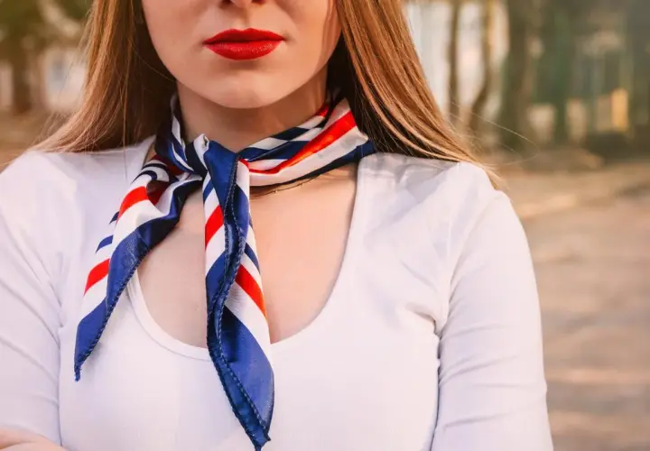 Kobieta w białej koszuli i apaszce w paski. Dowiedz się, jak nosić apaszkę do koszuli, by wyglądać stylowo.