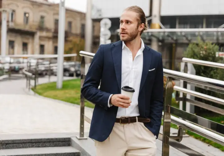 Mężczyzna w stylu smart casual z kawą w ręku, ubrany w granatową marynarkę i jasne spodnie, idzie po schodach.