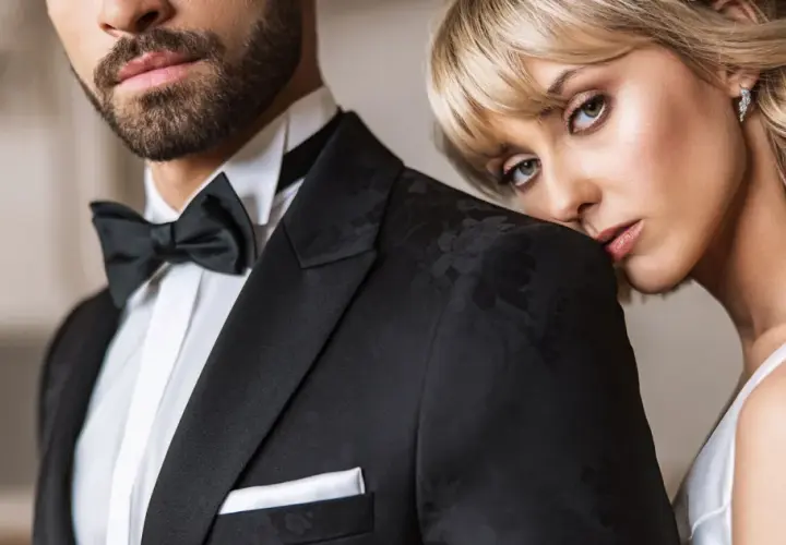 Elegancki mężczyzna w czarnym smokingu z muchą i białą koszulą. Kobieta opiera głowę na jego ramieniu. Idealny przykład, jaka koszula do muchy.