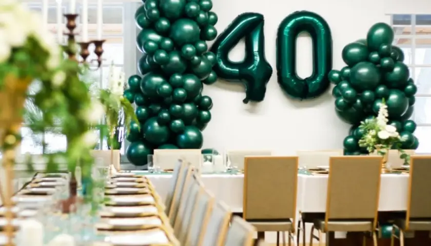 Uroczyste przyjęcie z okazji 40 urodzin w stylu lat 80. Zielone balony tworzą łuk z liczbą 40. Stoły nakryte do kolacji.
