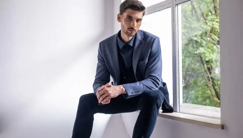 Elegancki mężczyzna w granatowej koszuli i garniturze, zastanawia się, jakie spodnie do niebieskiej koszuli będą najlepsze.