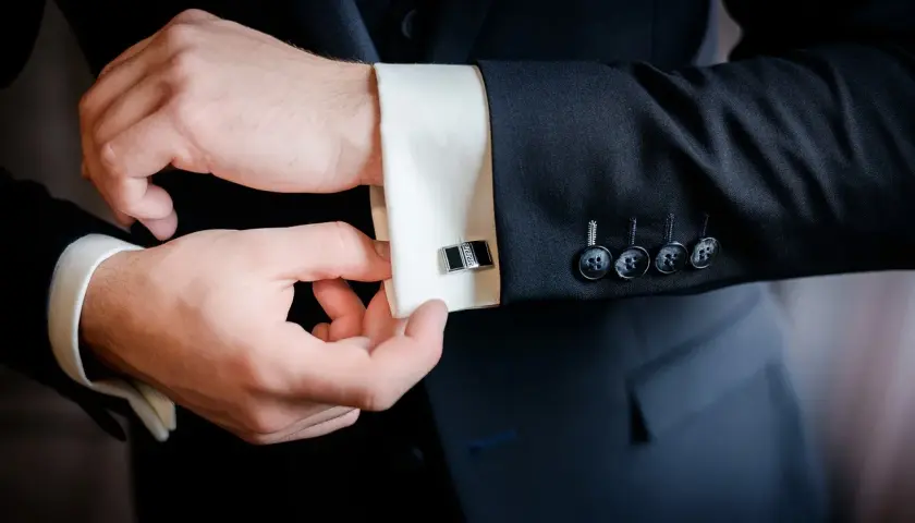 Mężczyzna zapina mankiet koszuli, pokazując, jak założyć spinki do koszuli. Elegancki detal dopełnia stylizację.