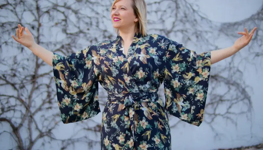 Kobieta w kimonie w styl orientalny, z motywem ptaków i kwiatów, rozkłada ramiona.