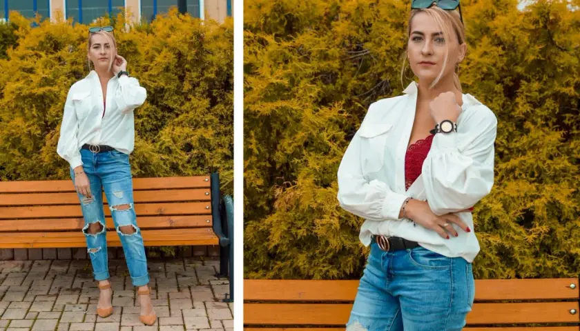 Kobieta w luźnej białej koszuli i podartych jeansach, z czerwoną koronkową braletką pod spodem, pozuje na tle żółtych krzewów.