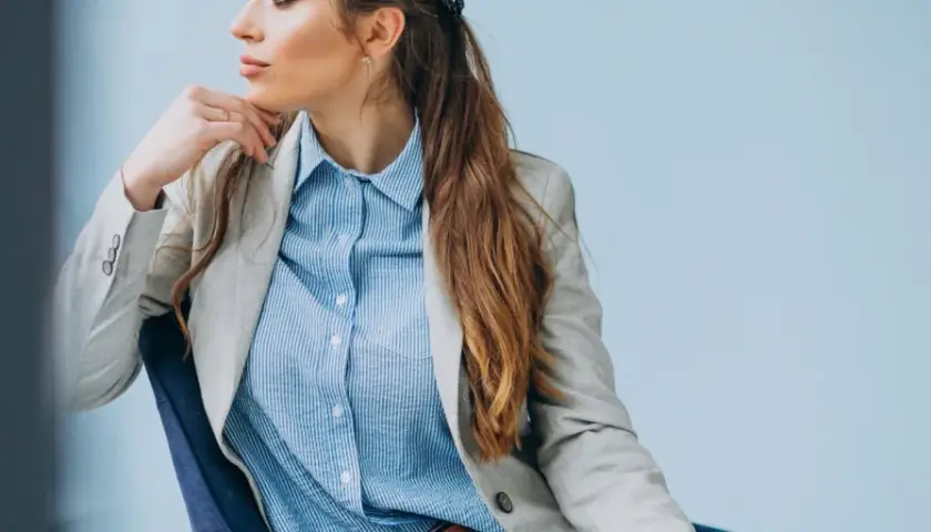 Elegancka kobieta w jasnej marynarce i błękitnej koszuli męskiej, tworząca stylową, biznesową stylizację.