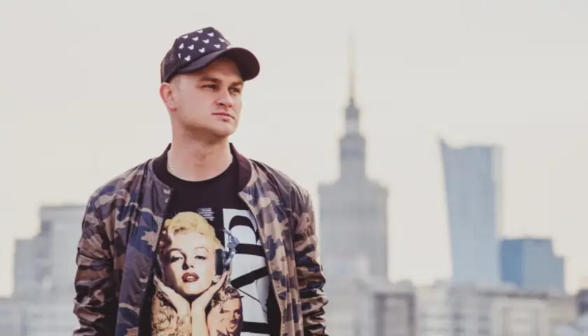 Młody mężczyzna w czapce z daszkiem i bluzie z Marilyn Monroe. Pokazuje, jak nosić czapkę z daszkiem w miejskim stylu.