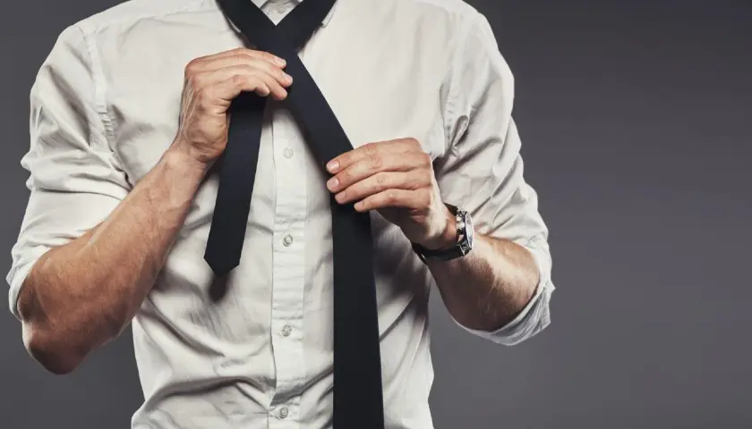Mężczyzna w białej koszuli wiąże czarny krawat. Prawidłowa długość krawata to klucz do eleganckiego wyglądu.