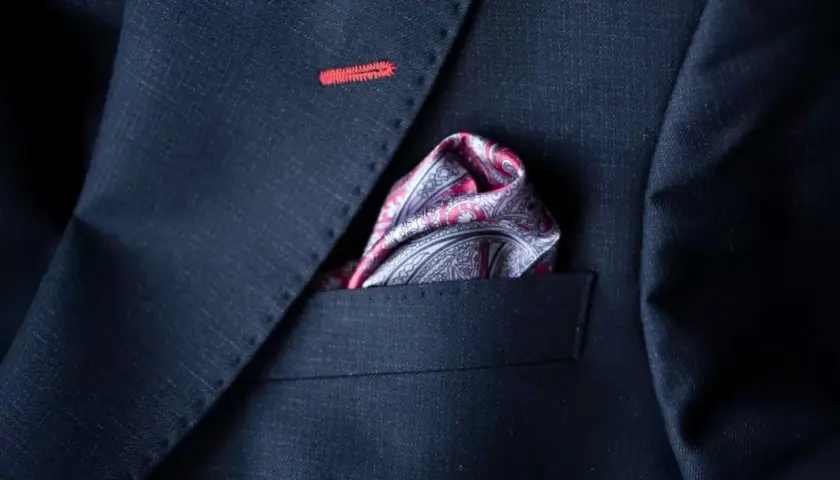 Elegancka poszetka w paisley do granatowego garnituru, z subtelnym czerwonym przeszyciem na klapie.
